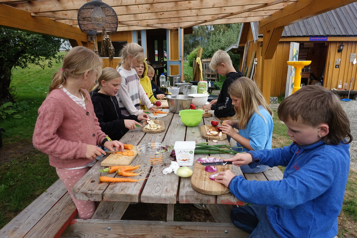 Barn kutter grønnsaker ved langbord utendørs